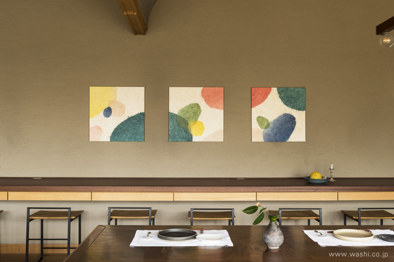 無垢材が優しく香るカフェ空間に、心を躍らせるカラフルな３連アートパネル。色とりどりの千切り和紙のコラージュが、温かみのある珪藻土の壁をより華やかに彩ります。