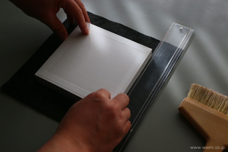 和紙アートパネルの制作風景。下貼りしたパネルに、定規を当てて加飾和紙を貼る位置を正確に決めている。