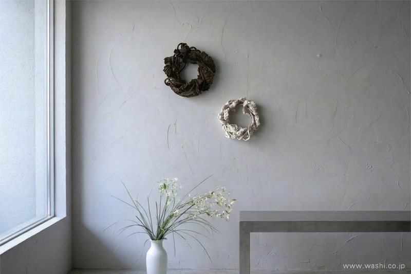 自然光が差し込むミニマルな空間の壁面に飾られた、リース型のモダンな和紙アート