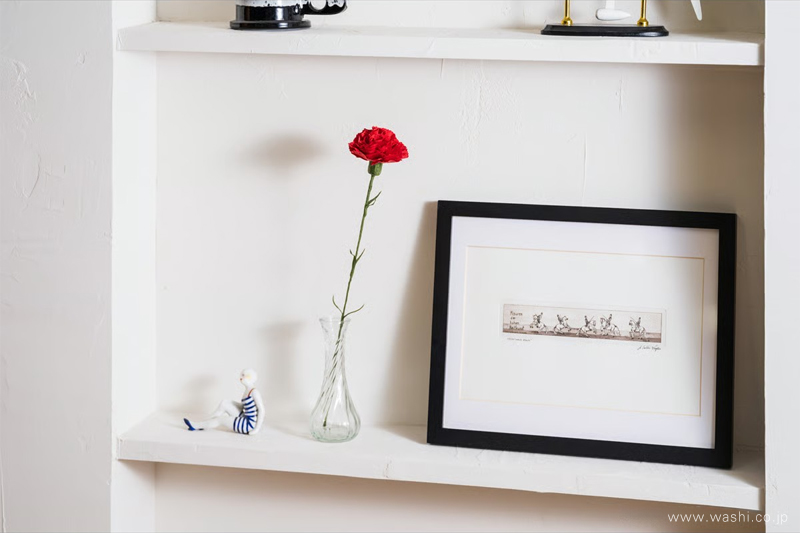 白い飾り棚のガラス花瓶に飾られた、赤色の和紙製カーネーション